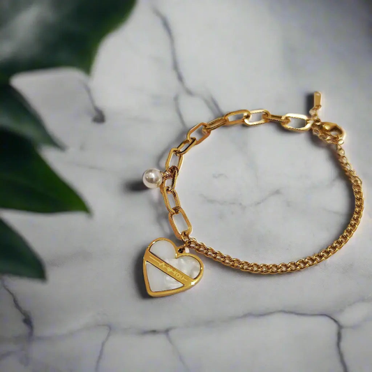 Gold heart charm bracelet with pearl accent and mixed chain links on marble surface