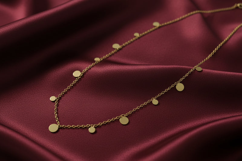 Elegant 18k gold plated stainless steel necklace featuring delicate disc pendants on a silky maroon background