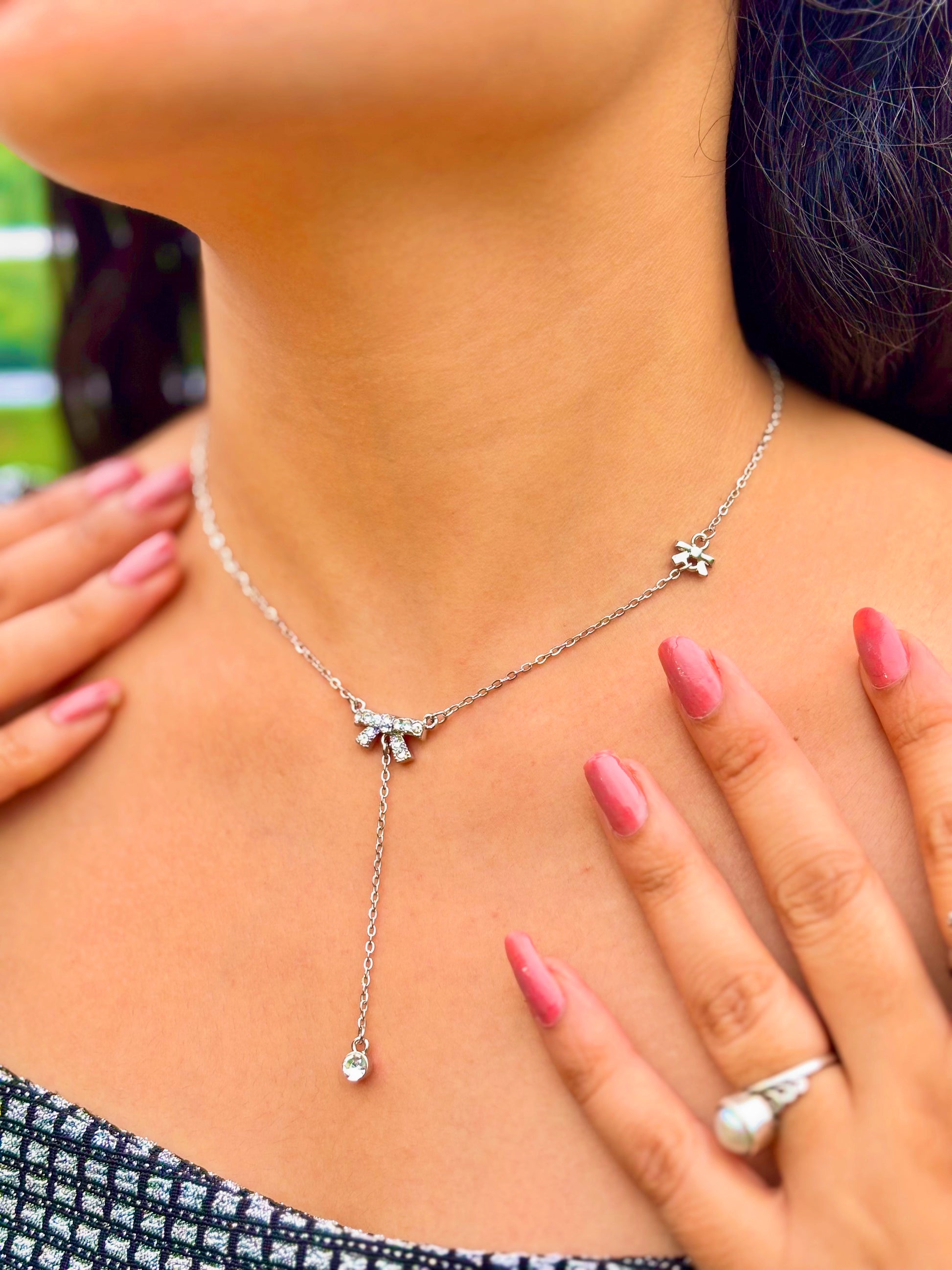 Silver bow charm necklace with delicate chain worn by woman with pink nail polish