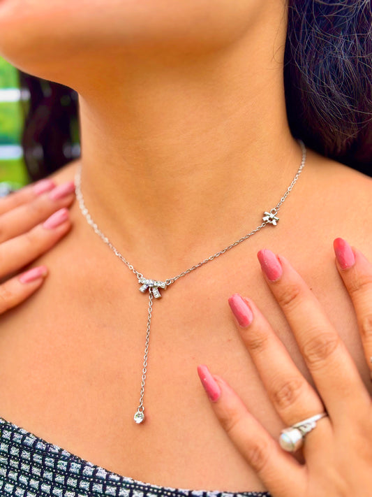 Silver bow charm necklace with delicate chain worn by woman with pink nail polish