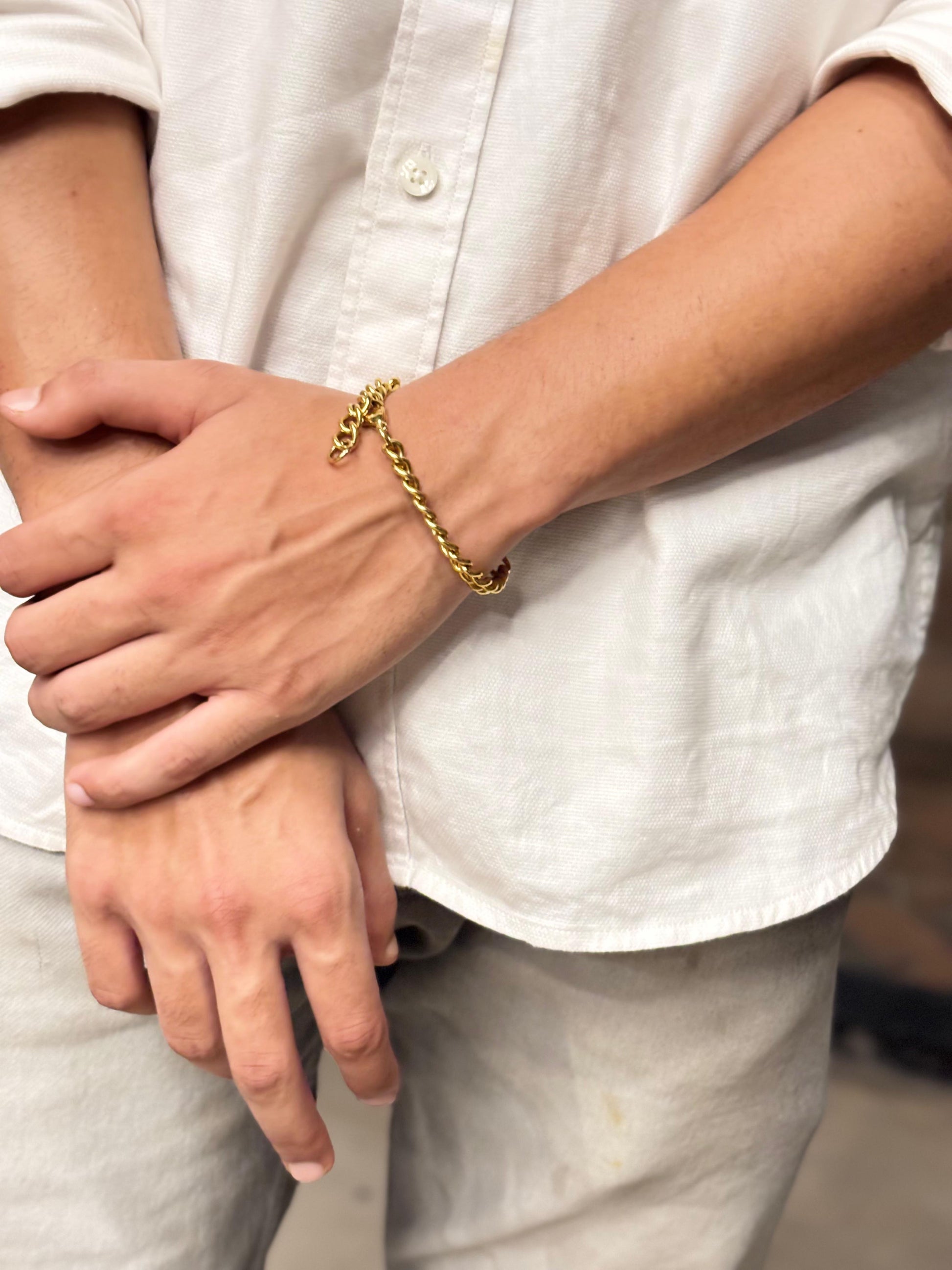 Lustre of Love gold bar bracelet on wrist with chunky chain worn with casual white shirt and linen pants