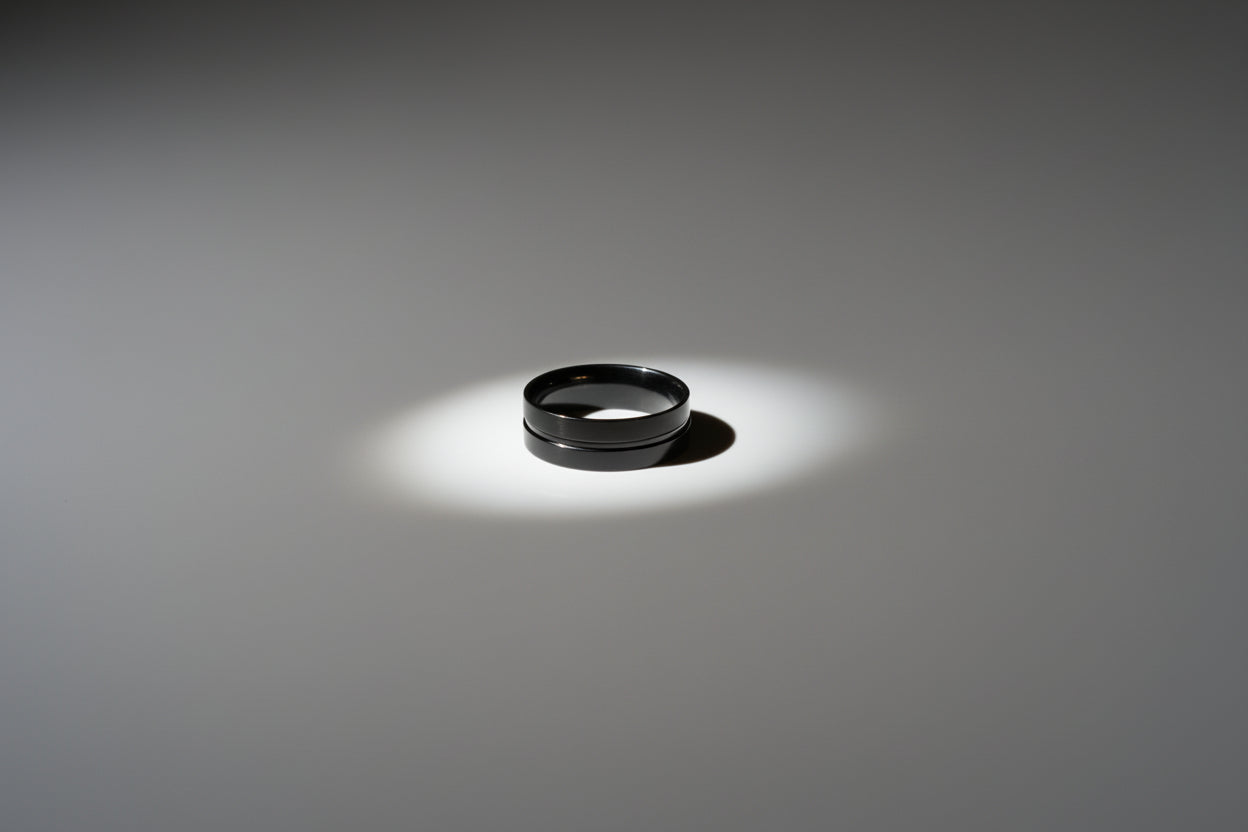 Simple black stainless steel ring on a smooth grey surface with subtle lighting