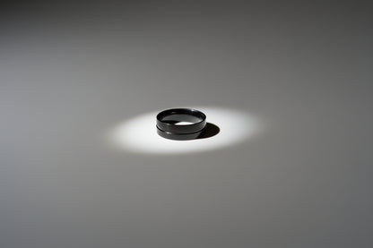 Simple black stainless steel ring on a smooth grey surface with subtle lighting