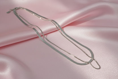 Elegant dual layer silver chain necklace laid flat on soft pink fabric for a stylish look
