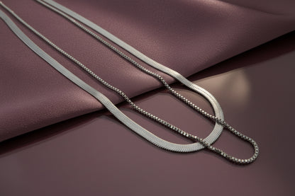 Elegant dual layer silver chain necklace displayed on soft fabric surface in muted tones