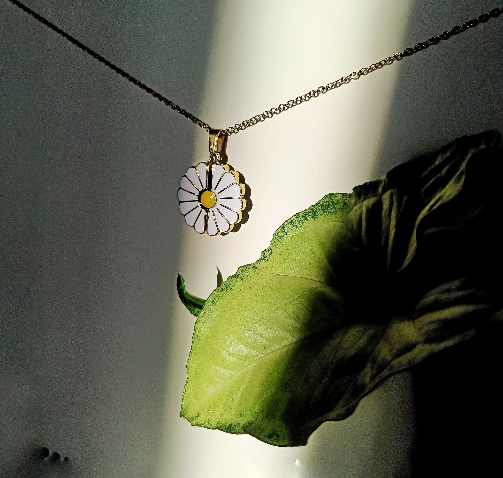 Lustre of Love custom daisy pendant necklace with white petals and yellow center hanging beside a green leaf
