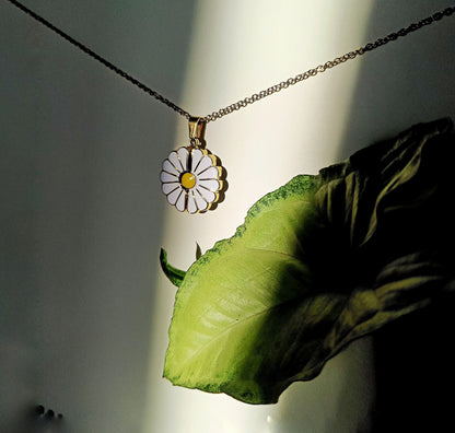 Lustre of Love custom daisy pendant necklace with white petals and yellow center hanging beside a green leaf