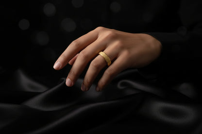 Elegant gold stainless steel ring displayed on a hand against a dark, softly textured background