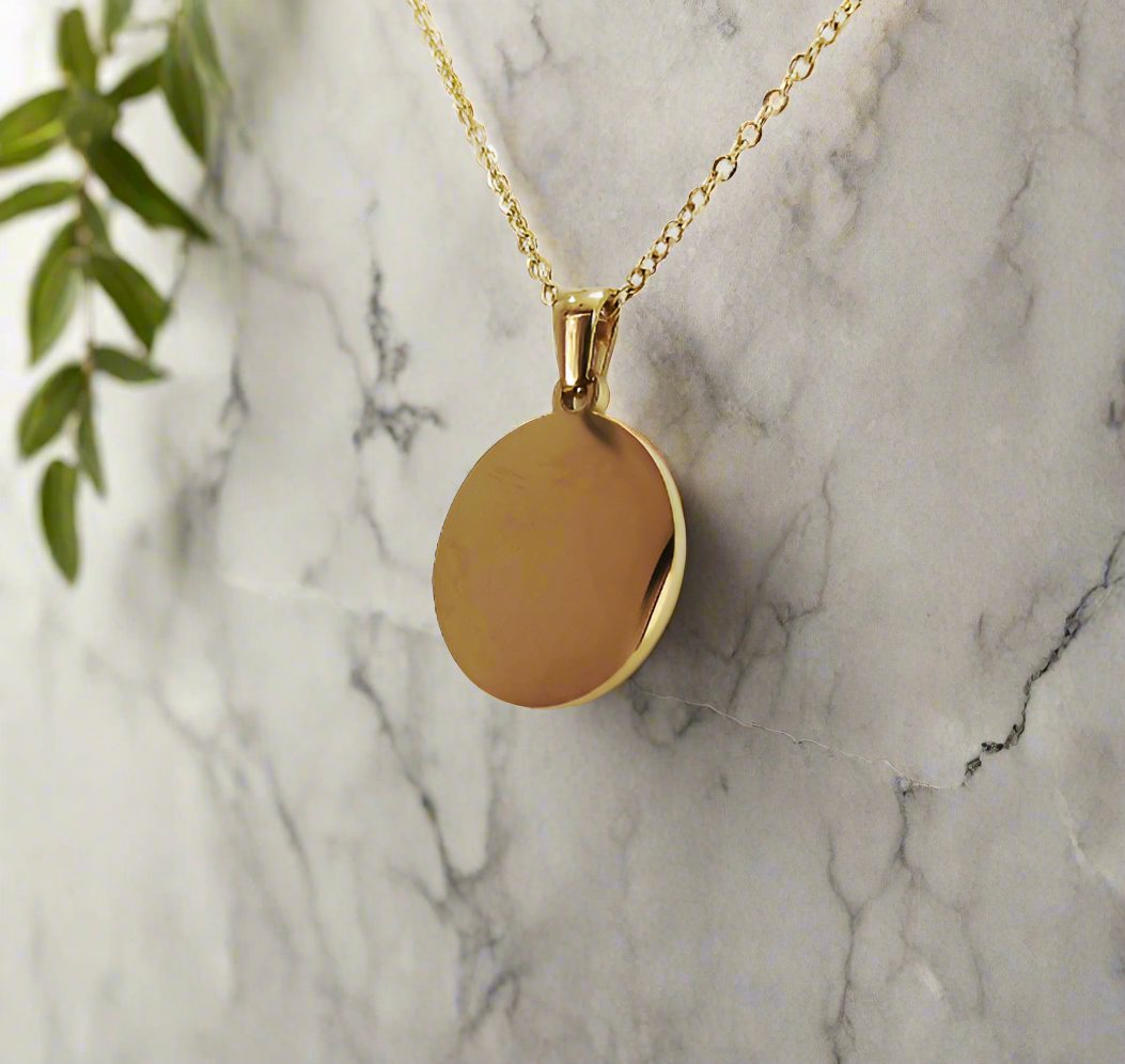 Gold custom round pendant necklace with smooth polished surface hanging against marble background