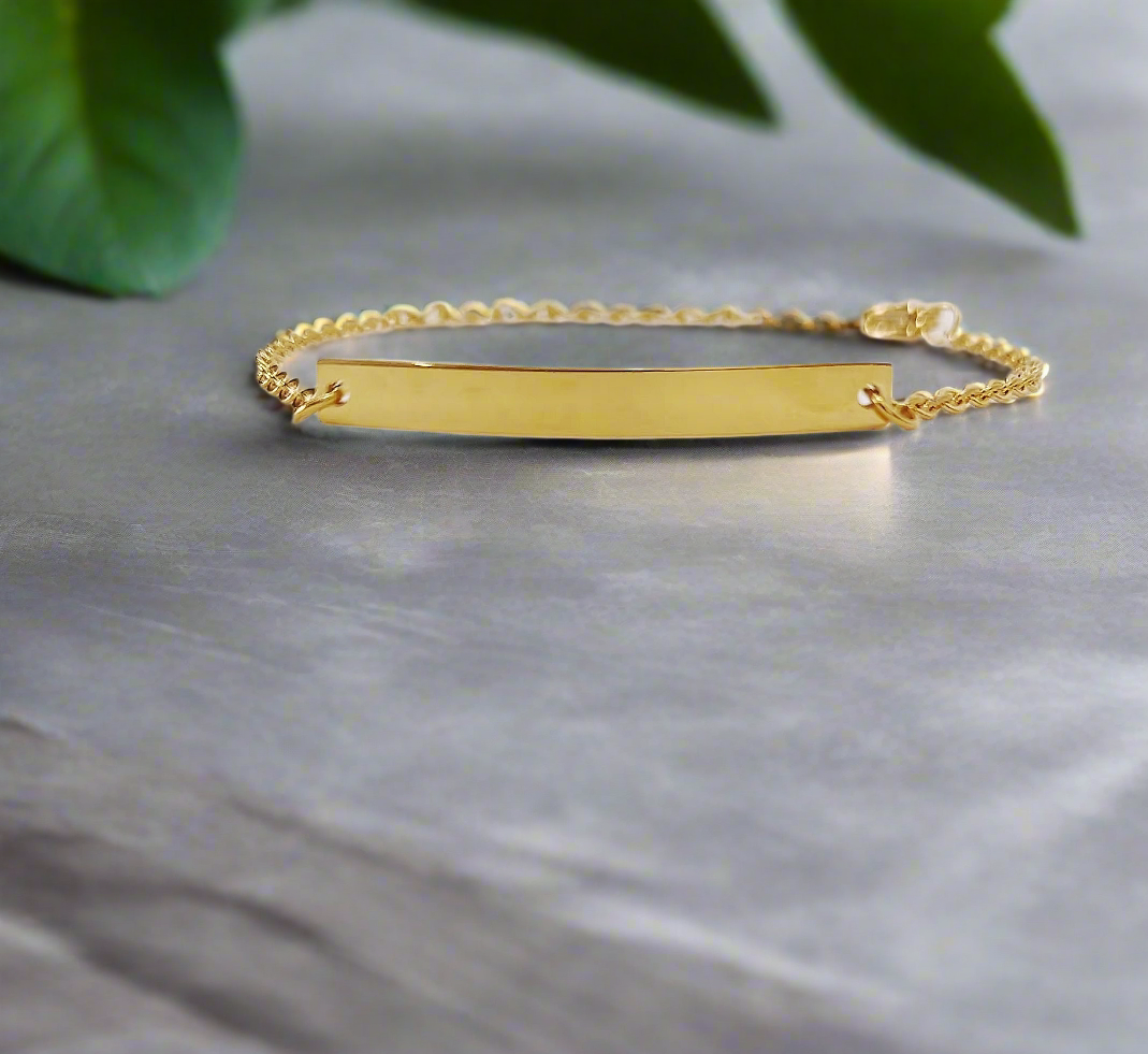 Lustre of Love elegant gold bar bracelet with a delicate chain on gray surface and green leaves background