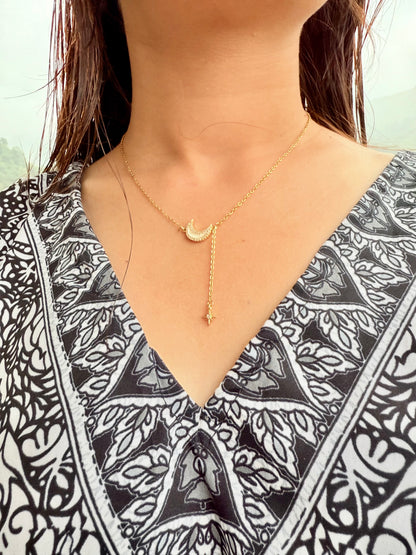 Gold moon pendant necklace with dangling star charm by Lustre of Love worn with patterned black and white top